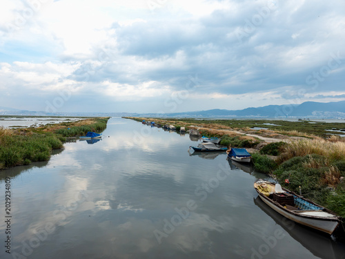 Fishing boats lining narrow wetland canal under cloudy sky