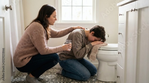 Adult comforting young person feeling unwell and nauseous in a bathroom with a glass of water, depicting care and illness.