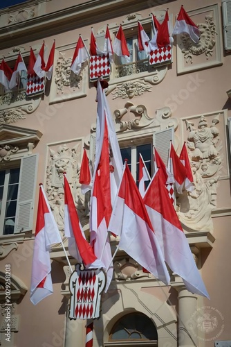 National flag of Monaco waving on a flagpole in Monte Carlo with trees and buildings in background