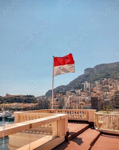 National flag of Monaco waving on a flagpole in Monte Carlo with trees and buildings in background