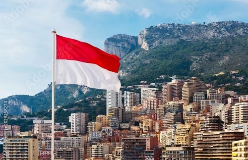 National flag of Monaco waving on a flagpole in Monte Carlo with trees and buildings in background