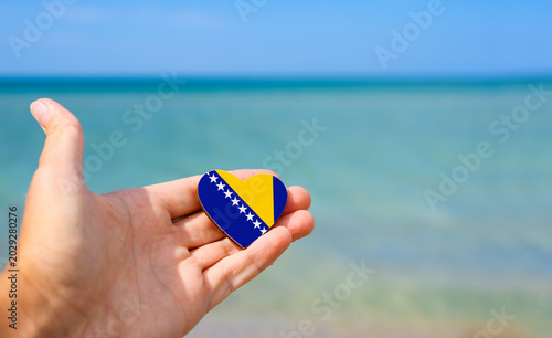 Flag of Bosnia and Herzegovina in hand against the sea. Summer vacation in Bosnia and Herzegovina