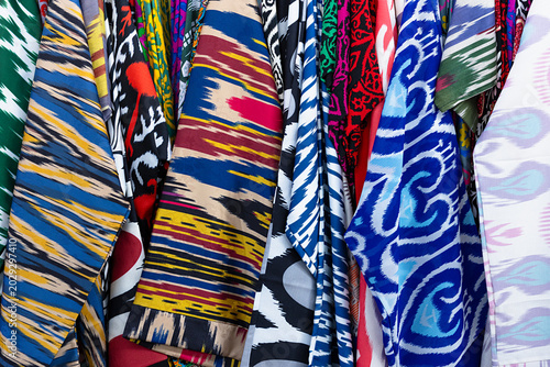 Colorful ikat fabrics hanging at Siab bazaar in Samarkand, displaying traditional Uzbek textile patterns. Ideal for travel, culture, and craft-related projects.