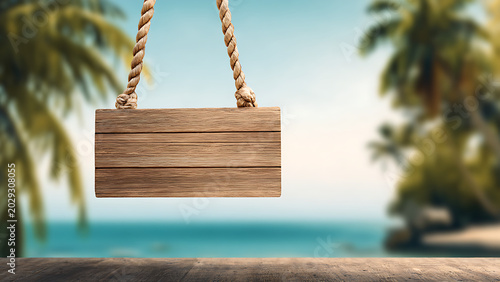 A blank wooden sign hangs by ropes in front of a blurred tropical beach scene.