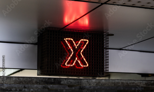 Photos Night photo of an illuminated red neon X symbol inside a metal security cage, signalling a restricted entry point or closed lane in a city parking station