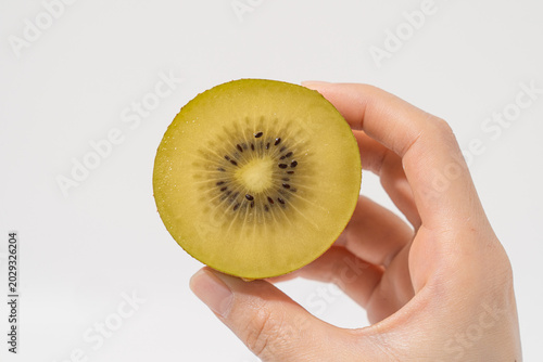 Hand holding a half slice of fresh golden kiwi fruit isolated on a white background