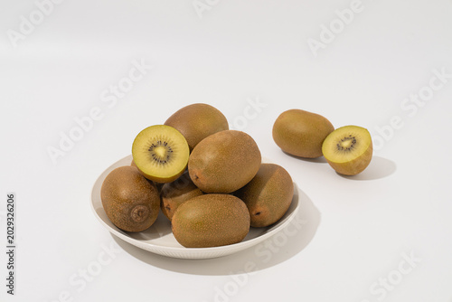 Pile of fresh golden kiwis on a white plate with a sliced half, isolated on a white background with hard shadow