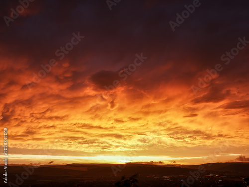 Fotografi Fiery mammatus thunderstorm clouds over landscape at sunset