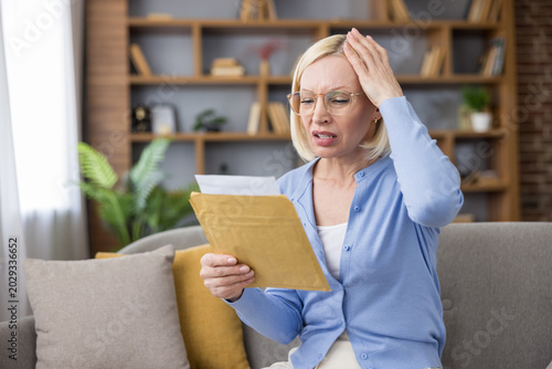 Foto Stressed mature woman sitting on a sofa, receiving bad news from a financial or