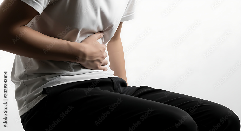 Obraz premium A man sitting and clutching his stomach in severe pain or cramp against a bright white background.