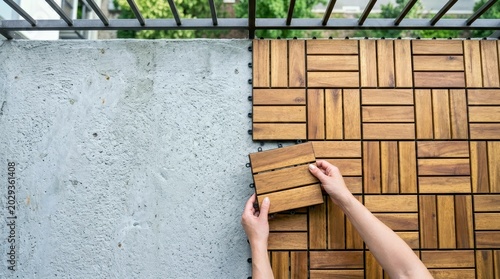 Person Installing Interlocking Wood Deck Tiles on Concrete Balcony Floor for Outdoor Patio Home Improvement Project