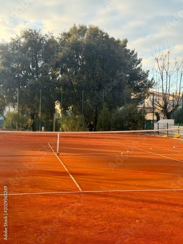 High angle view of a clay tennis court with net and warm sunset shadows
