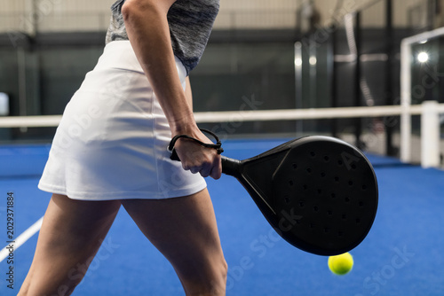 Fotografie Mature female wearing white skirt preparing to swing on blue court with black ra