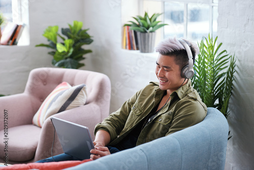 Laptop  headphones and Asian man in home for music  streaming video or watch show on internet. Computer  person and listening to audio in living room  movie and relax with podcast for happiness