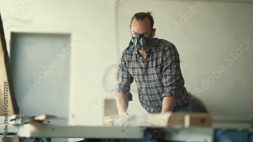 Carpenter with respirator mask sawing wood plank