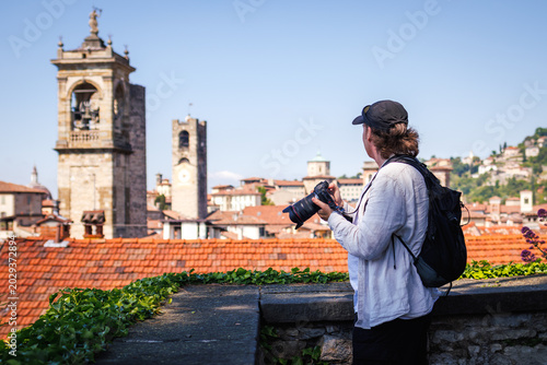 Solo traveler with camera photographing city skyline in Citta Alta, Bergamo, Italy during city break vacation. Summer holiday in Europe