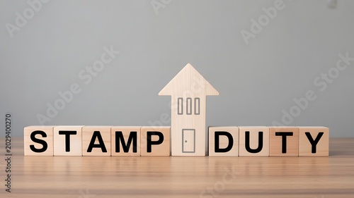 A wooden house model sits on blocks spelling 'STAMP DUTY' on a table.