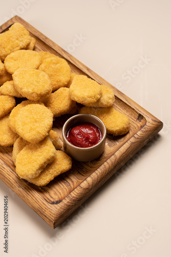 Chicken nuggets on wooden board over light beige background, crispy fast food snack concept
