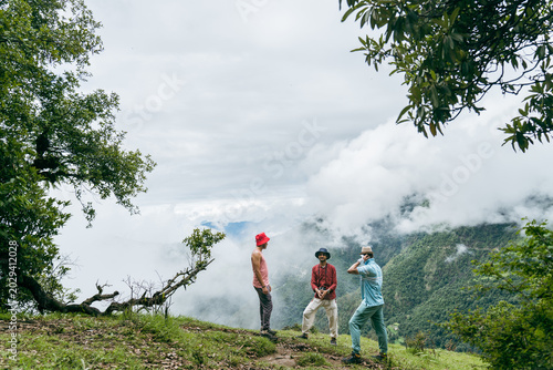 Fotografie Group of hikers standing on a grassy ridge overlooking misty mountain valleys at