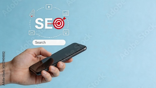 Hand holding smartphone with SEO search engine optimization concept, target arrow, video play button, analytics chart, lightbulb idea, email icon, representing digital marketing