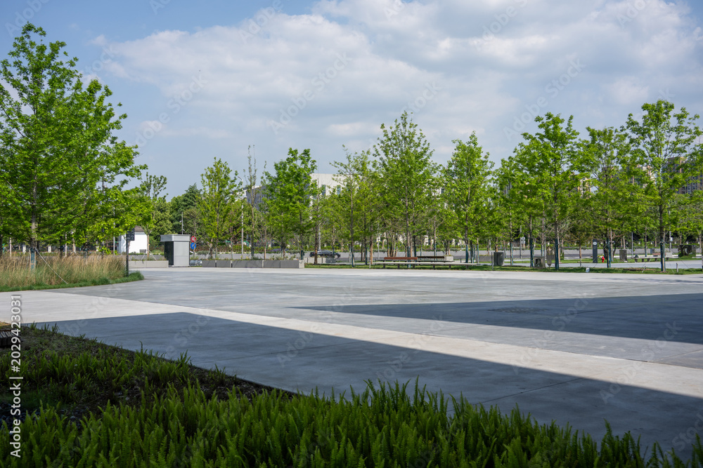 Fototapeta premium urban park square with green trees and lawn under blue sky