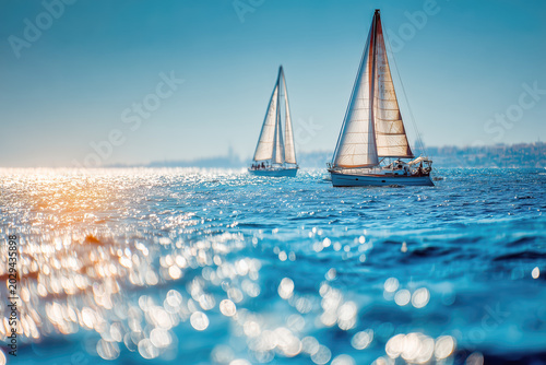 Two sailboats gliding across bright shimmering blue water