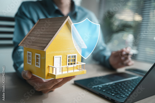 Agent holding model house with shield icon, showing home insurance, property coverage, mortgage protection, risk policy, and real estate finance concept.