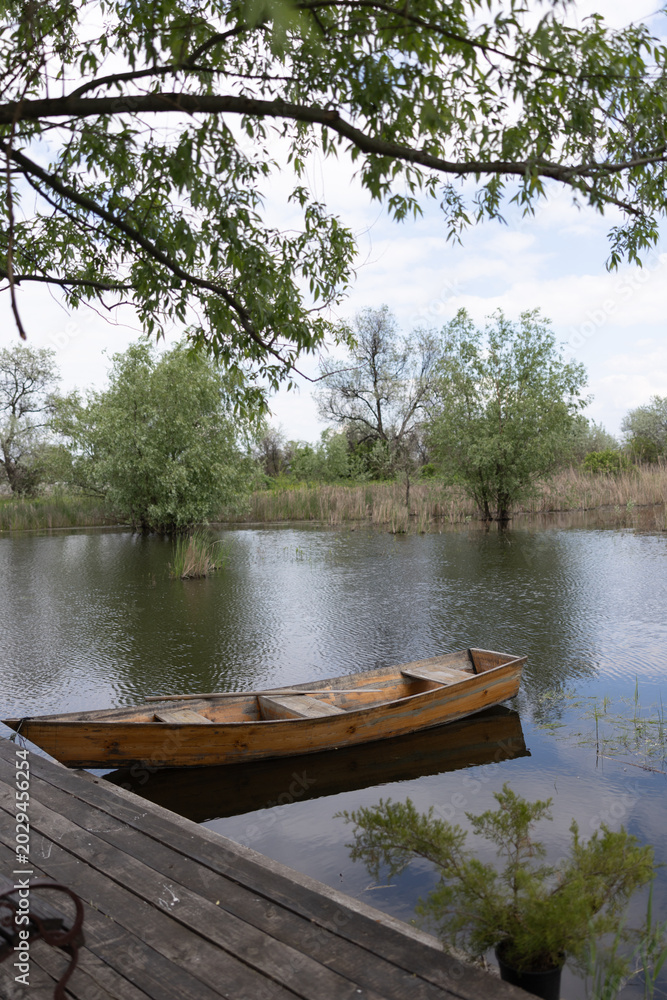 Fototapeta premium Wooden rowboat floating on calm lake water near pier