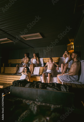 Group of young people relaxing and recovering in a large dry wooden sauna with a stone heater