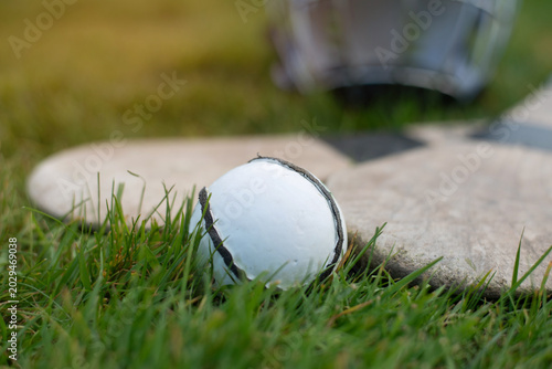 A hurling ball and two hurleys lie in grass after a game, and a helmet to protect the head during the game in the background, the Irish national game of Hurling and Camogie