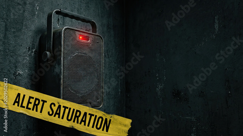 Alert saturation concept with black speaker emitting red warning light on dark textured wall, creating tense and urgent atmosphere