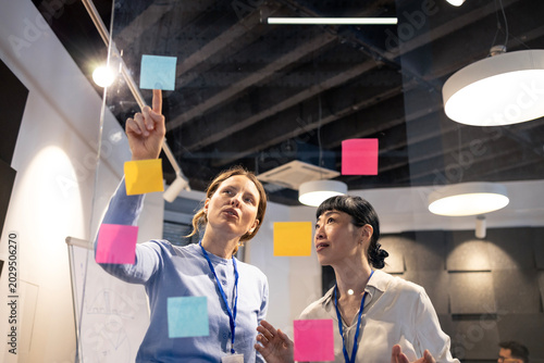 Foto Businesswomen collaborating on glass wall with sticky notes, organizing ideas du