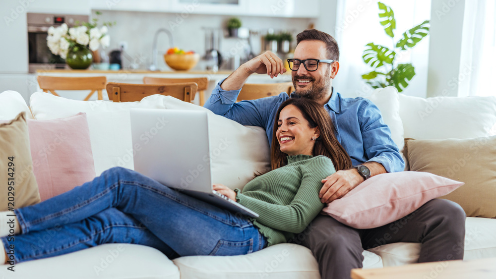Obraz premium Happy Couple Relaxing on Couch With Laptop in Bright Modern Living Room at Home