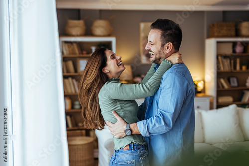 Happy Young Couple Embracing and Laughing Together in Cozy Living Room At Home