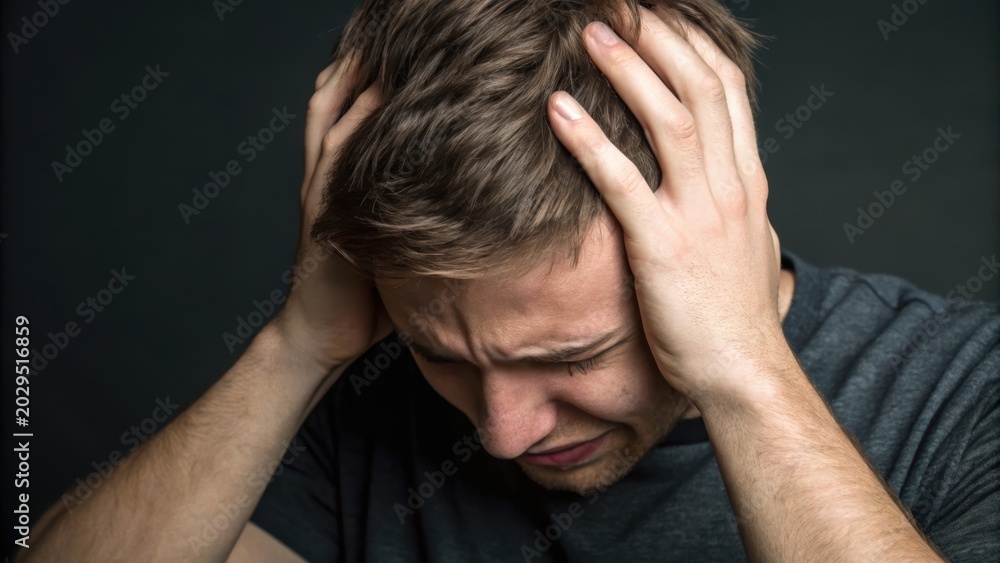 Fototapeta premium Man holding his head in distress, expressing pain or frustration against a dark background.