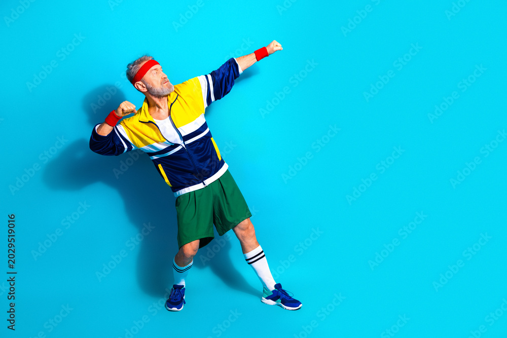 Obraz premium Energetic senior man in retro sportswear striking a victory pose against a bright blue background for fitness and active lifestyle