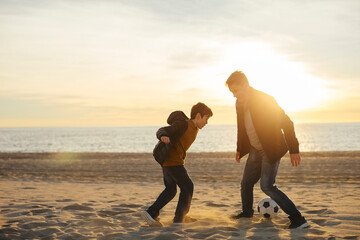 Father and son playing football on the beach at sunset