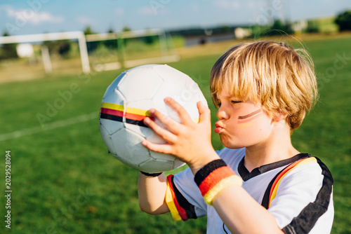Boy with face paint and German football shirt, kissing soccer ball