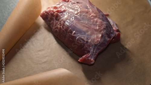 A person unwraps a package containing a raw meat cut on a clean surface.
