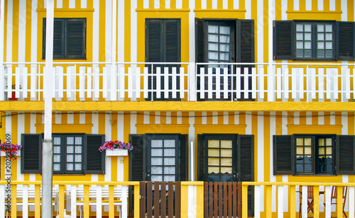Colorful Yellow Striped Portuguese Beach House Facade with Black Shutters and Flowers