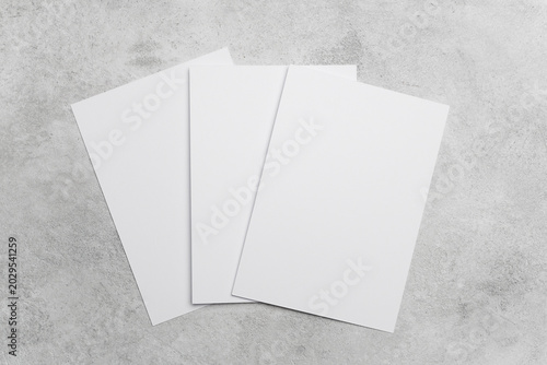 Three blank white sheets of paper arranged on a textured gray surface, ideal for design mockups or presentations