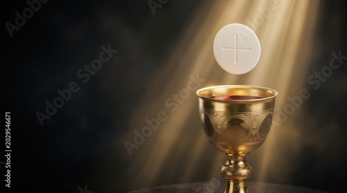 Golden chalice with red wine and a hovering communion wafer illuminated by a divine beam of light. Holy Eucharist and Christian sacrament concept. Dark textured background with copy space for text