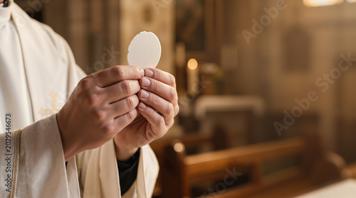 Close up of a priest's hands holding a communion wafer. Holy Eucharist sacrament during mass in a church. Copy space for text