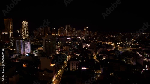 Nha Trang city skyline at sunset to night timelapse, Vietnam. Scenic evening aerial view of illuminated coastal resort city with skyscrapers, hotels, and traffic lights under dramatic clouds.