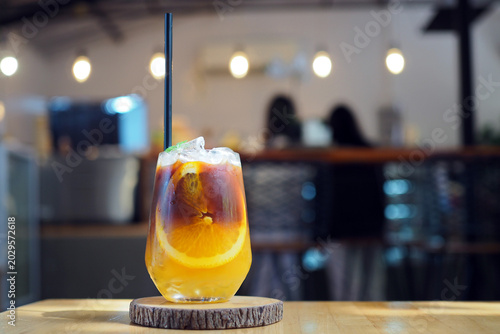 Foto A glass of iced americano coffee and layer of orange and lemon juice decorated with thyme leaf and sliced of orange on wooden coaster