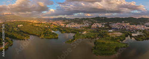 Canvas Print Panoramic drone photo of Tirana Lake, Albania, showing calm water, green parkland, city skyline, hills, and dramatic evening clouds