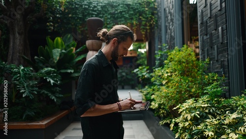 Bild auf Leinwand Man digital artist creating artwork on tablet in green tropical garden