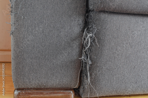 Worn sofa upholstery with torn seam and damaged fabric texture. Furniture repair and home wear concept