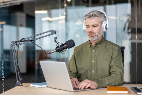 Bild auf Leinwand Mature man with headphones hosting a podcast in a home studio, speaking into a p