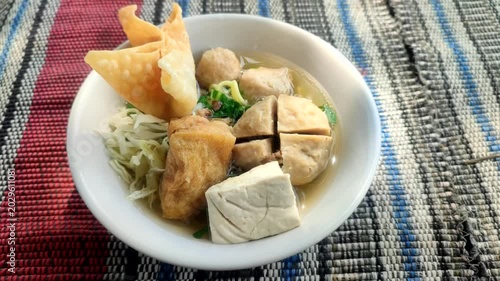 Close up video of delicious bakso meatball soup in white bowl on simple mat, authentic Indonesian street food with warm taste